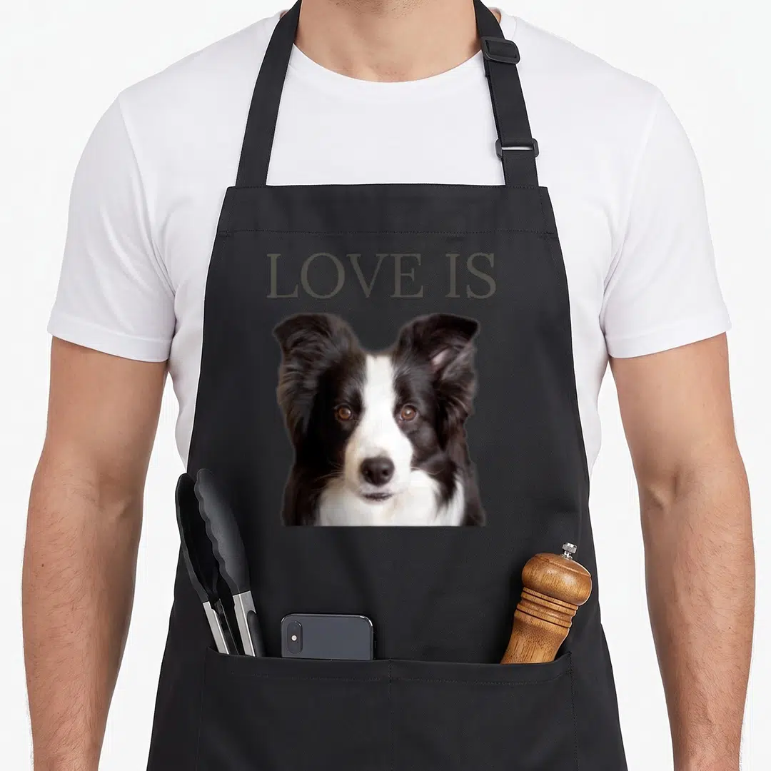 Retro dog border collie apron - LOVE IS text above a black white grey dog head photo on a grey background — shown on a black cotton canvas apron against a white background