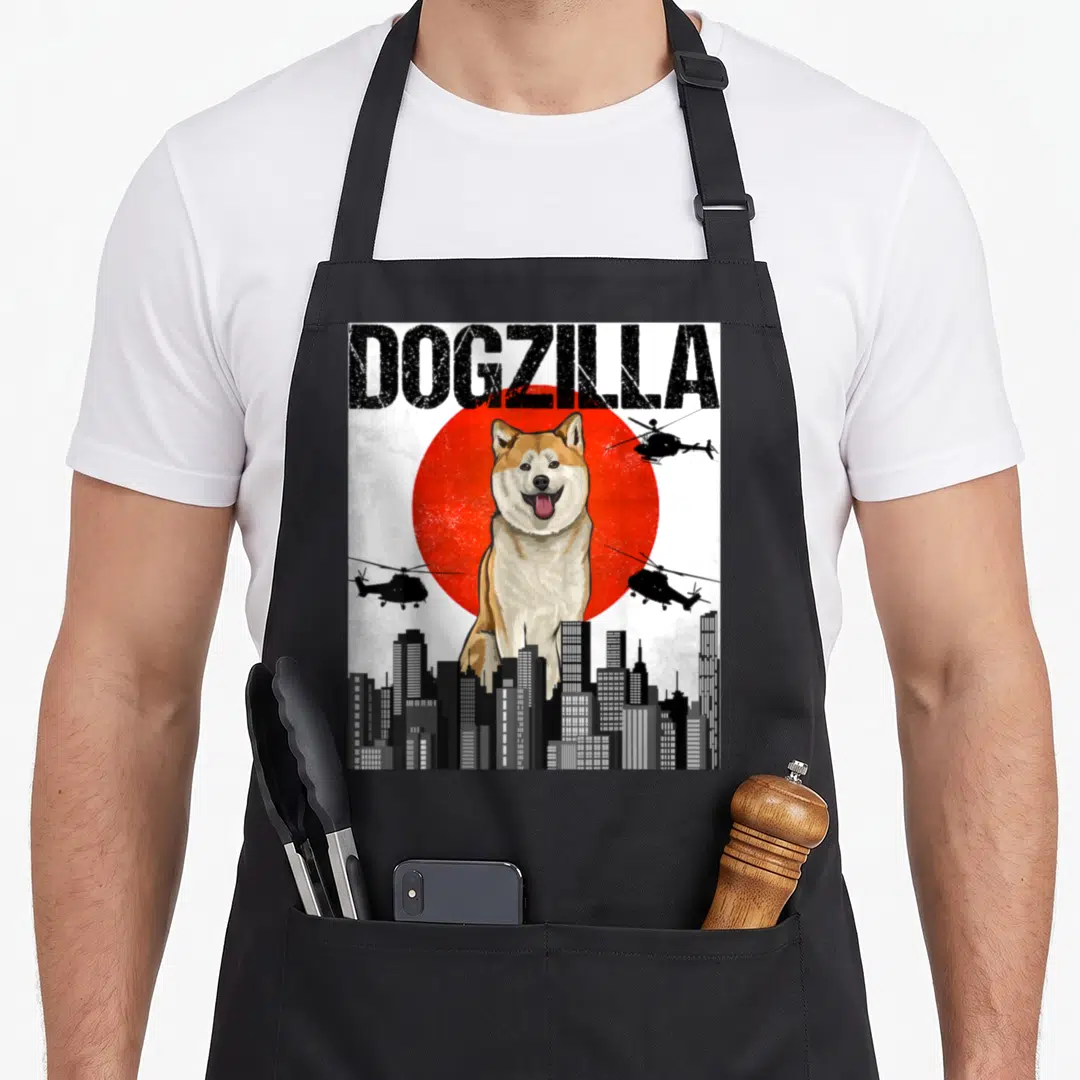 Japanese akita apron - DOGZILLA text over Shiba Inu, red sun, black helicopters, and city skyline in cartoon style — shown on a black cotton canvas apron against a white background