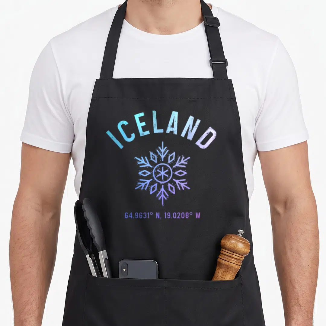 Souvenir icelandic apron - ICELAND text arched over a blue purple snowflake with Reykjavik coordinates below — shown on a black cotton canvas apron against a white background