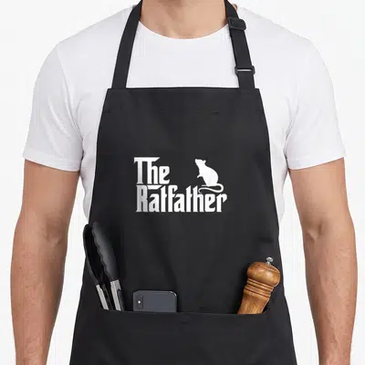 Owner rat dad apron - White The Ratfather text with a minimalist rat silhouette sitting on the lettering — shown on a black cotton canvas apron against a white background
