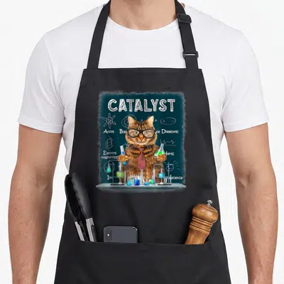 Catalyst cat apron - Realistic brown cat with glasses and tie holding lab flasks in front of teal chalkboard — shown on a black cotton canvas apron against a white background