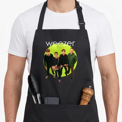Album novelty apron - Weezer text above four men standing in front of a lime green circle — shown on a black cotton canvas apron against a white background