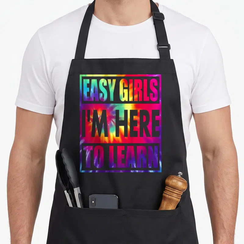 Kindergarten preschool apron - Grey block text reading Easy Girls I'm Here To Learn over multicolored tie-dye square — shown on a black cotton canvas apron against a white background
