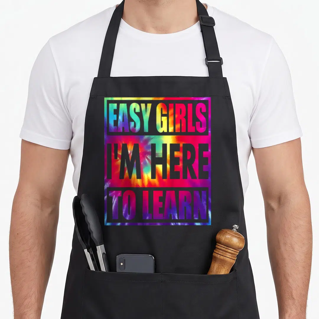 Kindergarten preschool apron - Grey block text reading Easy Girls I'm Here To Learn over multicolored tie-dye square — shown on a black cotton canvas apron against a white background