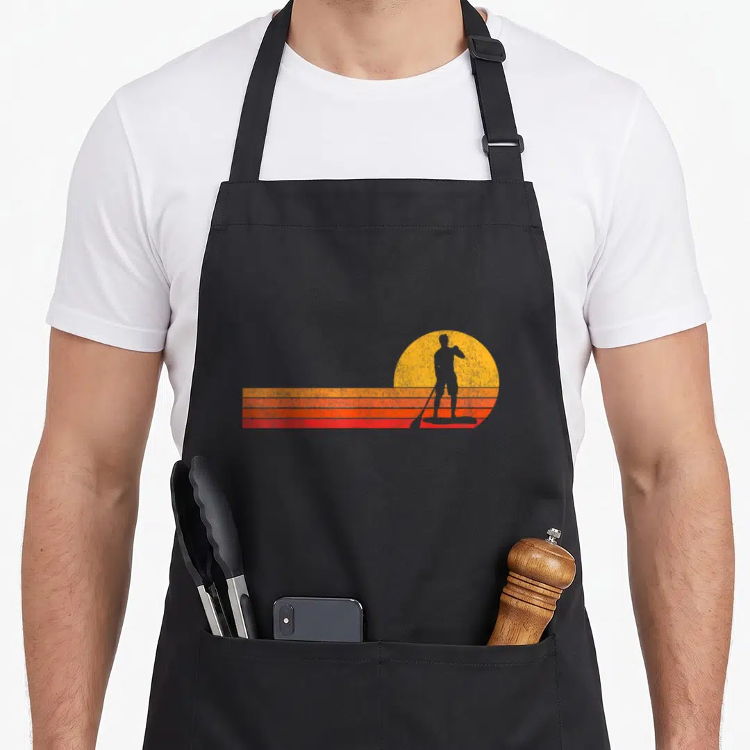 Board paddle apron - Retro paddleboarder silhouette against yellow sun with orange and red stripes — shown on a black cotton canvas apron against a white background