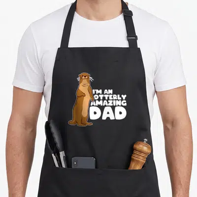 Sea father day apron - Brown cartoon otter standing next to white text I'm an Otterly Amazing Dad — shown on a black cotton canvas apron against a white background