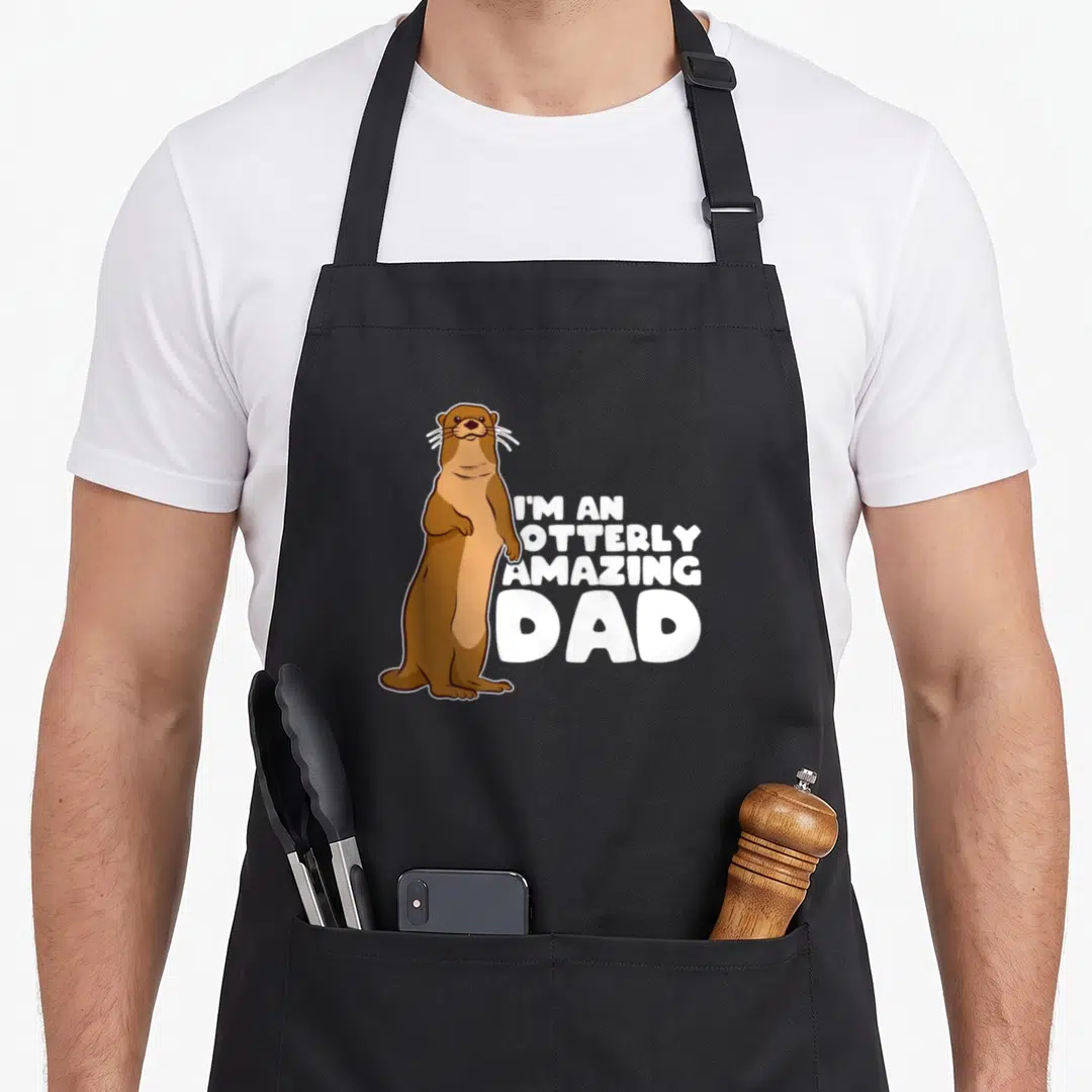 Sea father day apron - Brown cartoon otter standing next to white text I'm an Otterly Amazing Dad — shown on a black cotton canvas apron against a white background