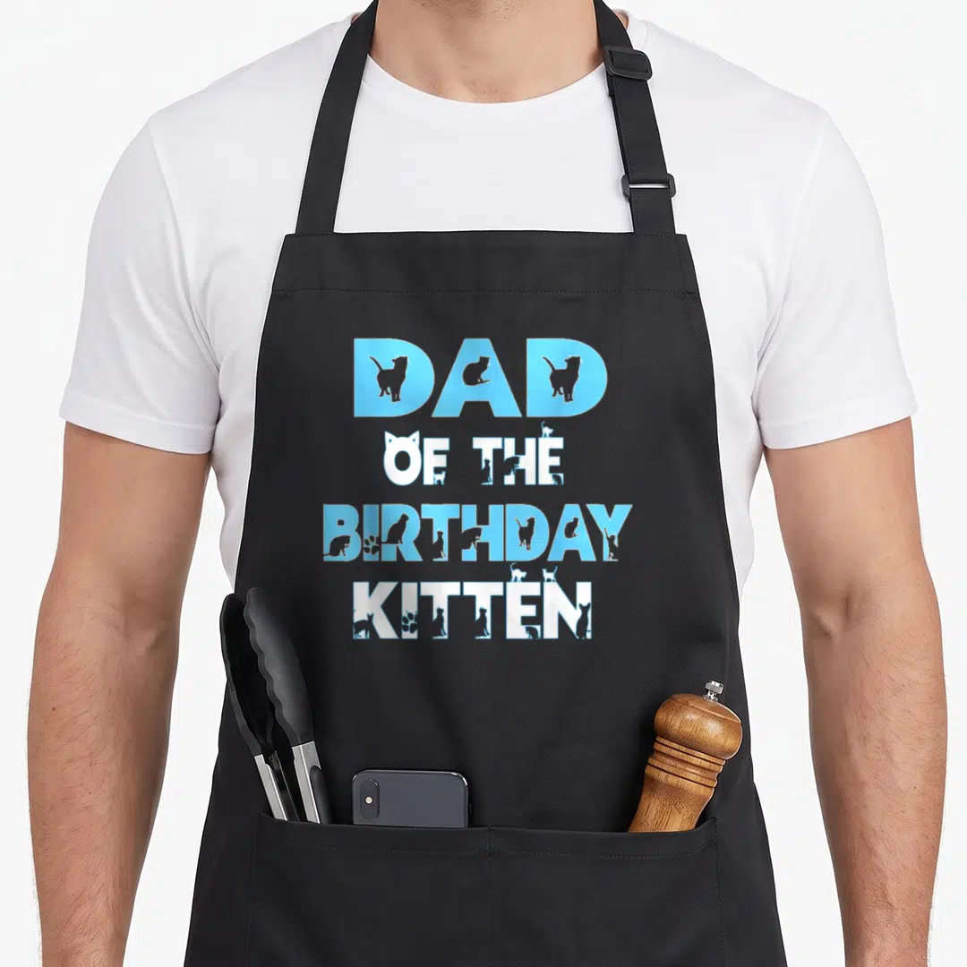 Kitten themed cat apron - Dad of the Birthday Kitten text with grey cat silhouettes in blue and white stacked typography — shown on a black cotton canvas apron against a white background