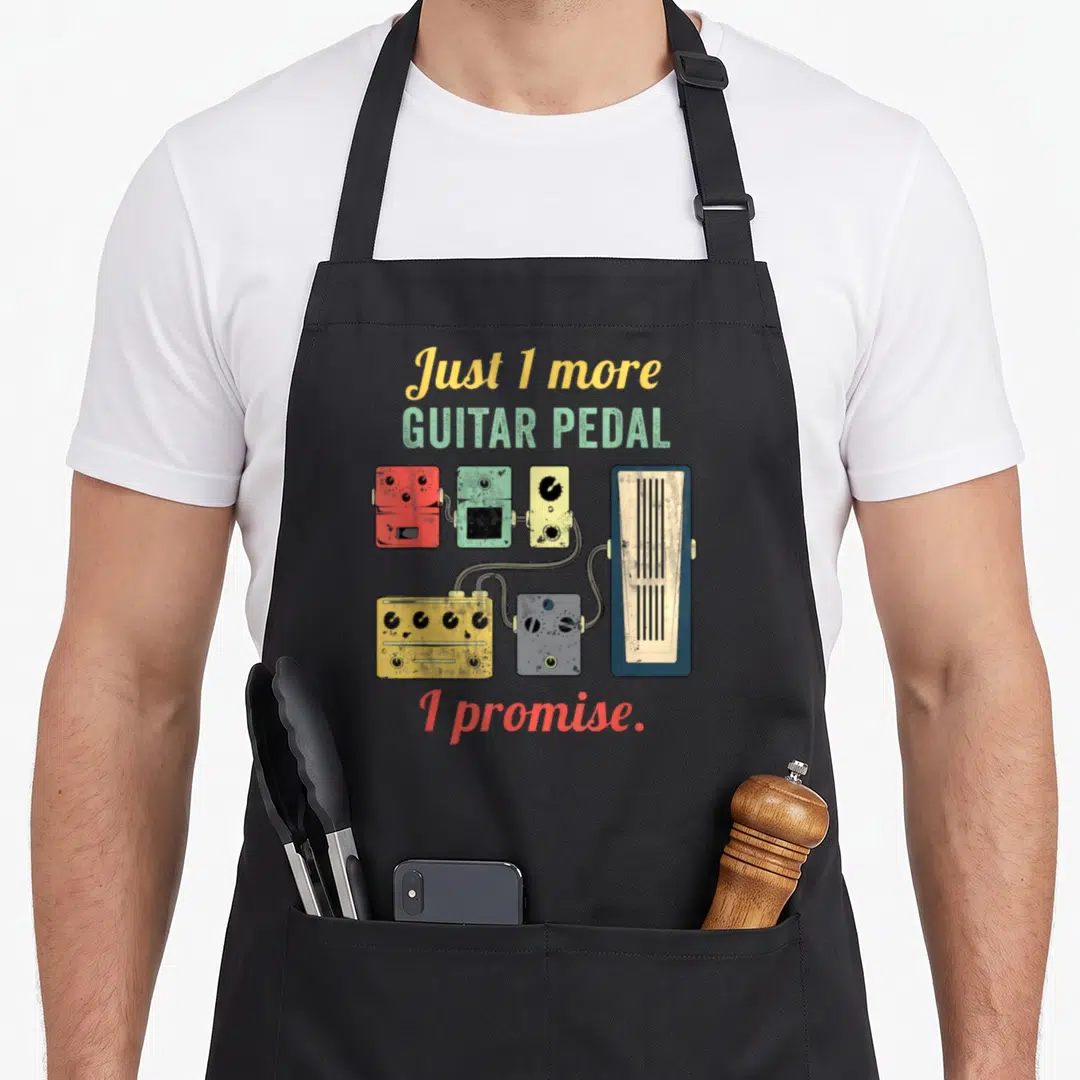 Amplifier crew apron - Cartoon guitar pedals in yellow green red and blue connected by cables under the text Just 1 — shown on a black cotton canvas apron against a white background
