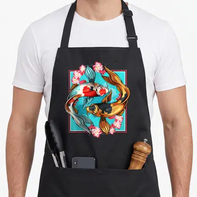 Nishikigoi japan apron - Two koi fish in a blue square frame surrounded by pink cherry blossoms in cartoon style — shown on a black cotton canvas apron against a white background