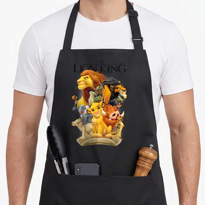 Land pride apron - Cartoon lions and text The Lion King clustered on a rock base — shown on a black cotton canvas apron against a white background