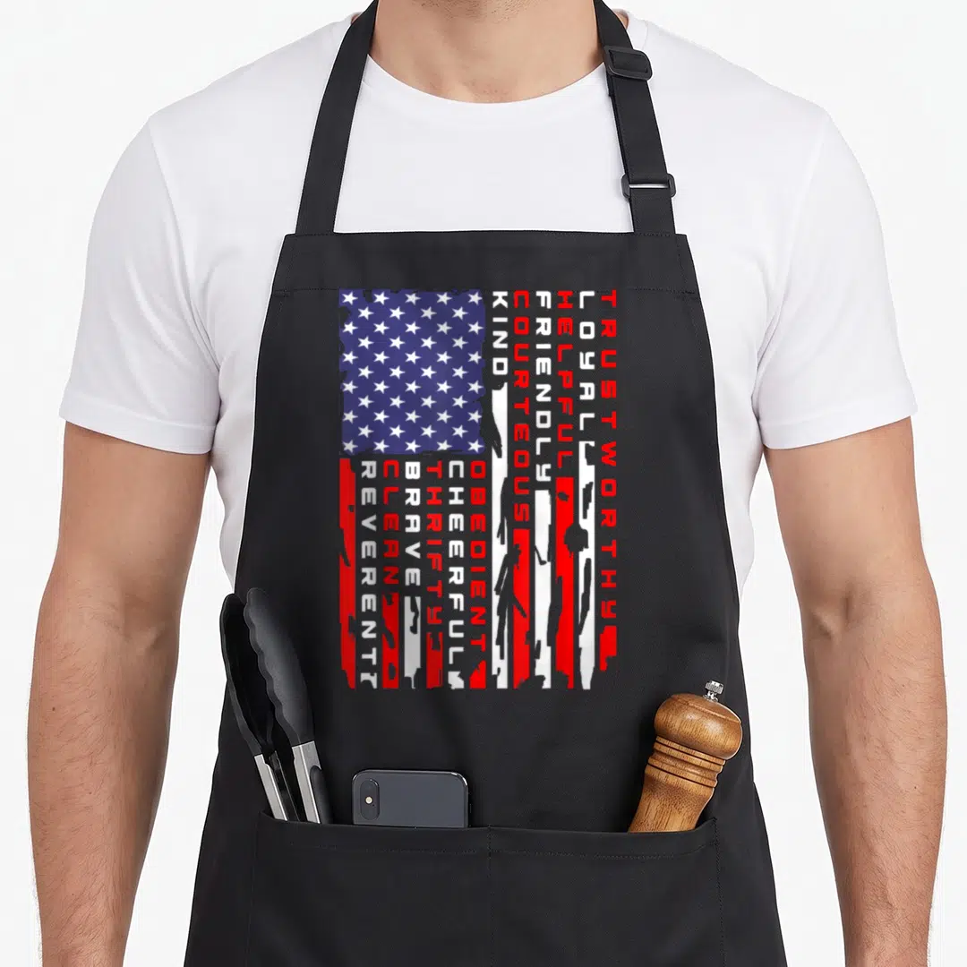 Scouting american flag apron - Distressed US flag design with vertical text reading Trustworthy Loyal Helpful Friendly — shown on a black cotton canvas apron against a white background