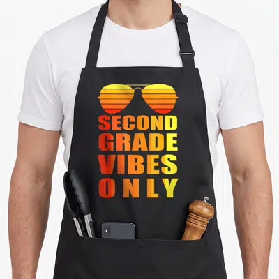 Second grade school 2nd apron - Retro sunglasses in red orange yellow gradient above stacked text SECOND GRADE VIBES — shown on a black cotton canvas apron against a white background