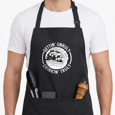 Gettin summer aprons - White circular wave design with bird and text GETTIN UNRULY DRINKIN TRULY — shown on a black cotton canvas apron against a white background