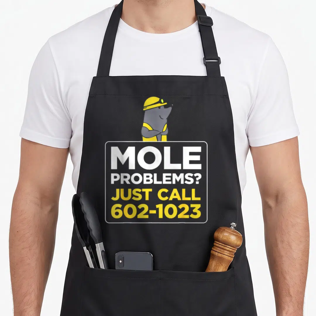 Problem mole apron - Cartoon mole in yellow hard hat above sign reading MOLE PROBLEMS JUST CALL 602-1023 — shown on a black cotton canvas apron against a white background