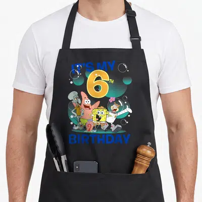 Squarepant 6th birthday apron - SpongeBob and friends cluster under IT'S MY 6TH BIRTHDAY text with scattered bubbles — shown on a black cotton canvas apron against a white background
