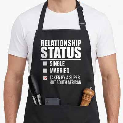 Relationship south african apron - White relationship status checklist with red checkmark next to taken by a super hot — shown on a black cotton canvas apron against a white background