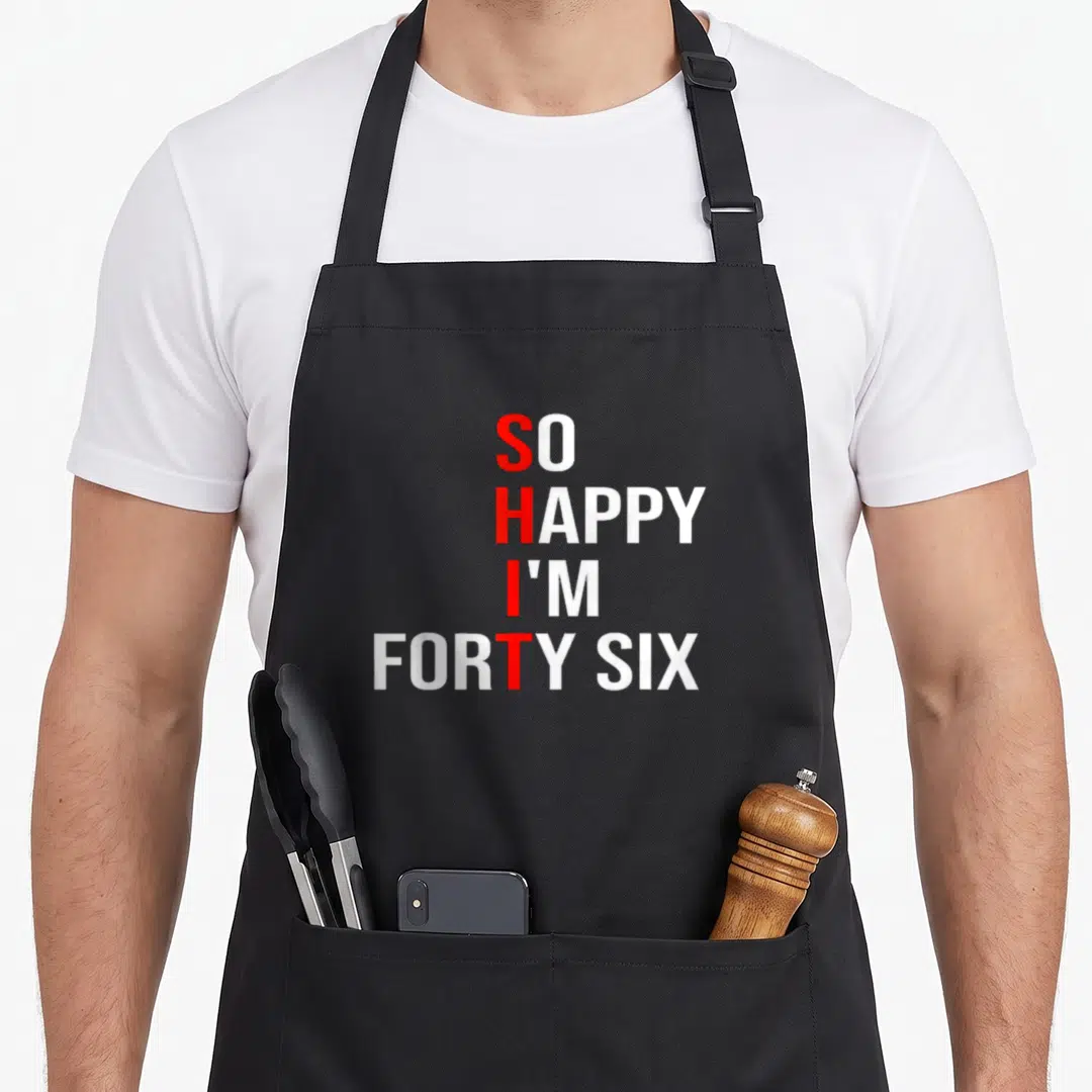 Forty six birthday apron - White text SO HAPPY I'M FORTY SIX with red S H I T vertical acronym — shown on a black cotton canvas apron against a white background