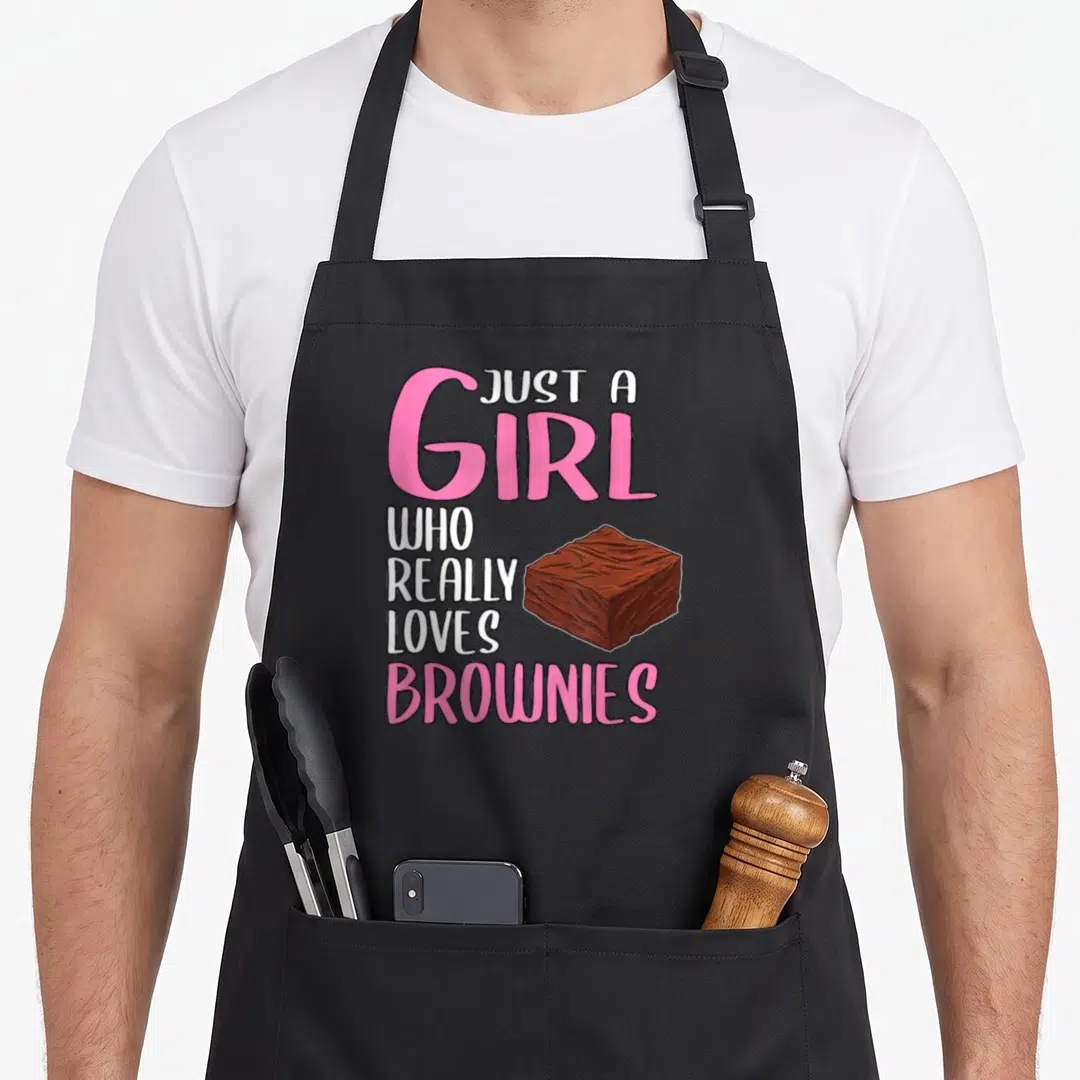 Brownie browny apron - Cartoon brownie next to stacked pink and white text reading Just A Girl Who Really Loves Brownies — shown on a black cotton canvas apron against a white background