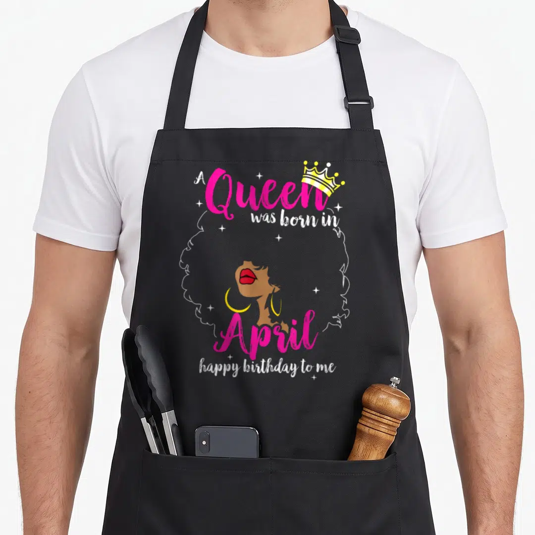 April baking queen apron - A Queen born in April text with brown profile white afro outline and yellow crown — shown on a black cotton canvas apron against a white background