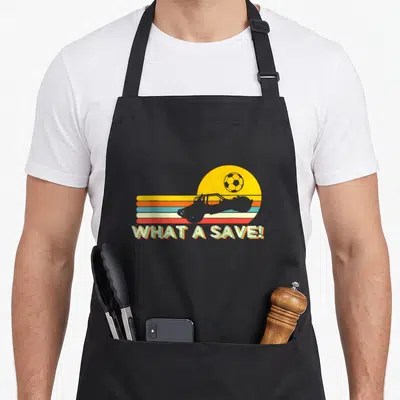 Rocket car apron - Retro off-road vehicle silhouette over yellow orange blue red stripes with What A Save text — shown on a black cotton canvas apron against a white background