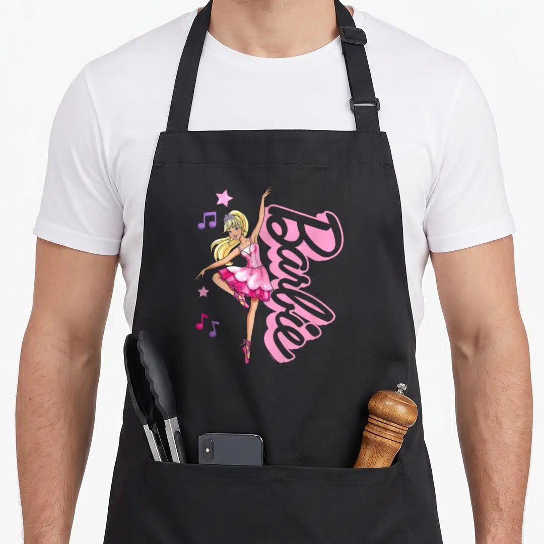 Retro ballet ballerina apron - Blonde cartoon doll in pink tutu dancing beside pink Barbie logo with purple notes — shown on a black cotton canvas apron against a white background