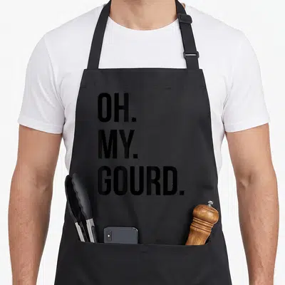 Gourd fall aprons - Stacked black text reading OH. MY. GOURD. in three lines — shown on a black cotton canvas apron against a white background