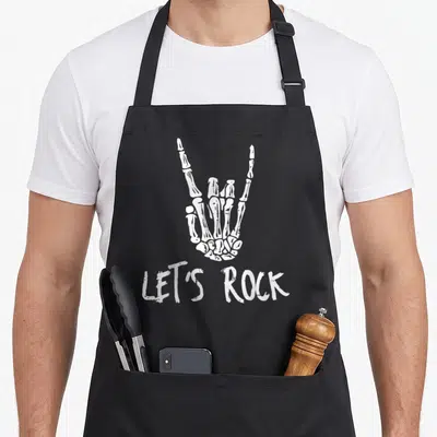 Youth punk rock apron - White distressed skeleton hand making rock gesture above LETS ROCK text — shown on a black cotton canvas apron against a white background