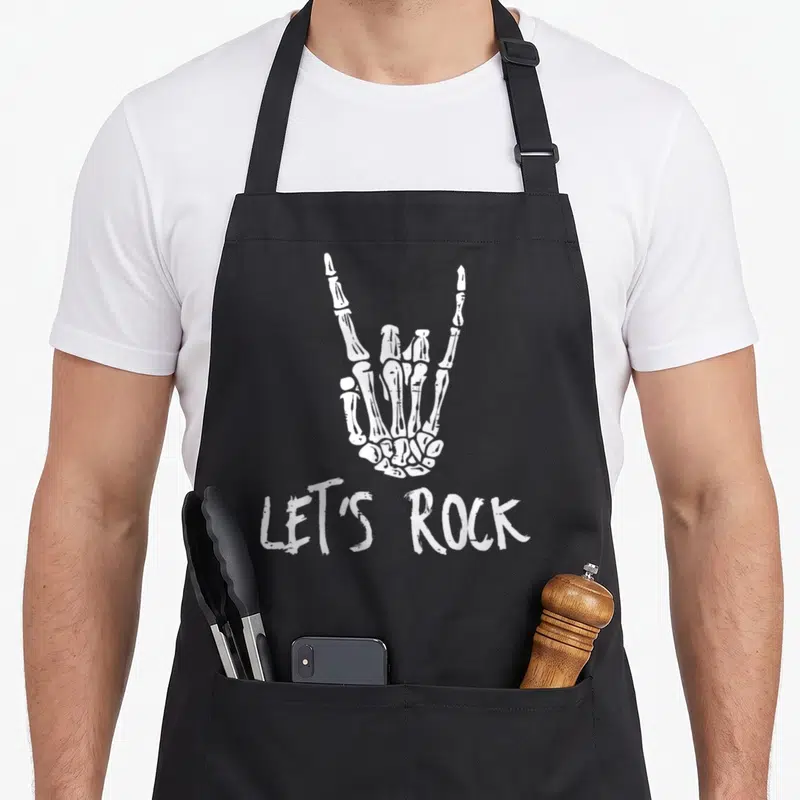 Youth punk rock apron - White distressed skeleton hand making rock gesture above LETS ROCK text — shown on a black cotton canvas apron against a white background