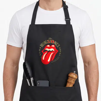 Tongue rolling stones apron for men - Red lips and tongue graphic with gold FIFTY YEARS text arching around it in white — shown on a black cotton canvas apron against a white background