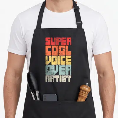 Funny artist voice acting apron - Stacked retro text reading SUPER COOL VOICE OVER ARTIST in red orange yellow blue — shown on a black cotton canvas apron against a white background