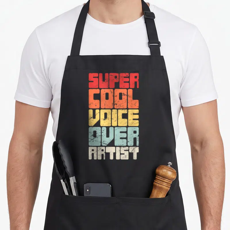 Funny artist voice acting apron - Stacked retro text reading SUPER COOL VOICE OVER ARTIST in red orange yellow blue — shown on a black cotton canvas apron against a white background