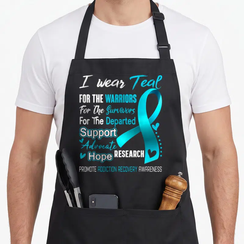 Awareness addiction recovery apron - Stacked white and teal text reading I wear Teal For The Warriors next to a large — shown on a black cotton canvas apron against a white background