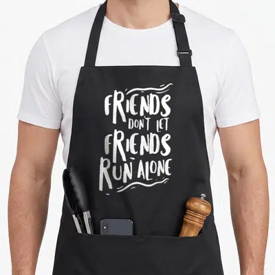 Running friends apron - White text FRIENDS DON'T LET FRIENDS RUN ALONE stacked vertically with squiggly lines on dark — shown on a black cotton canvas apron against a white background