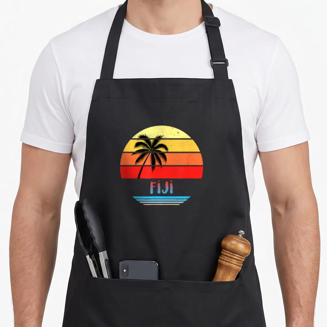 Funny souvenir fiji apron - Retro black palm tree silhouette against yellow orange red striped sun with blue Fiji text — shown on a black cotton canvas apron against a white background