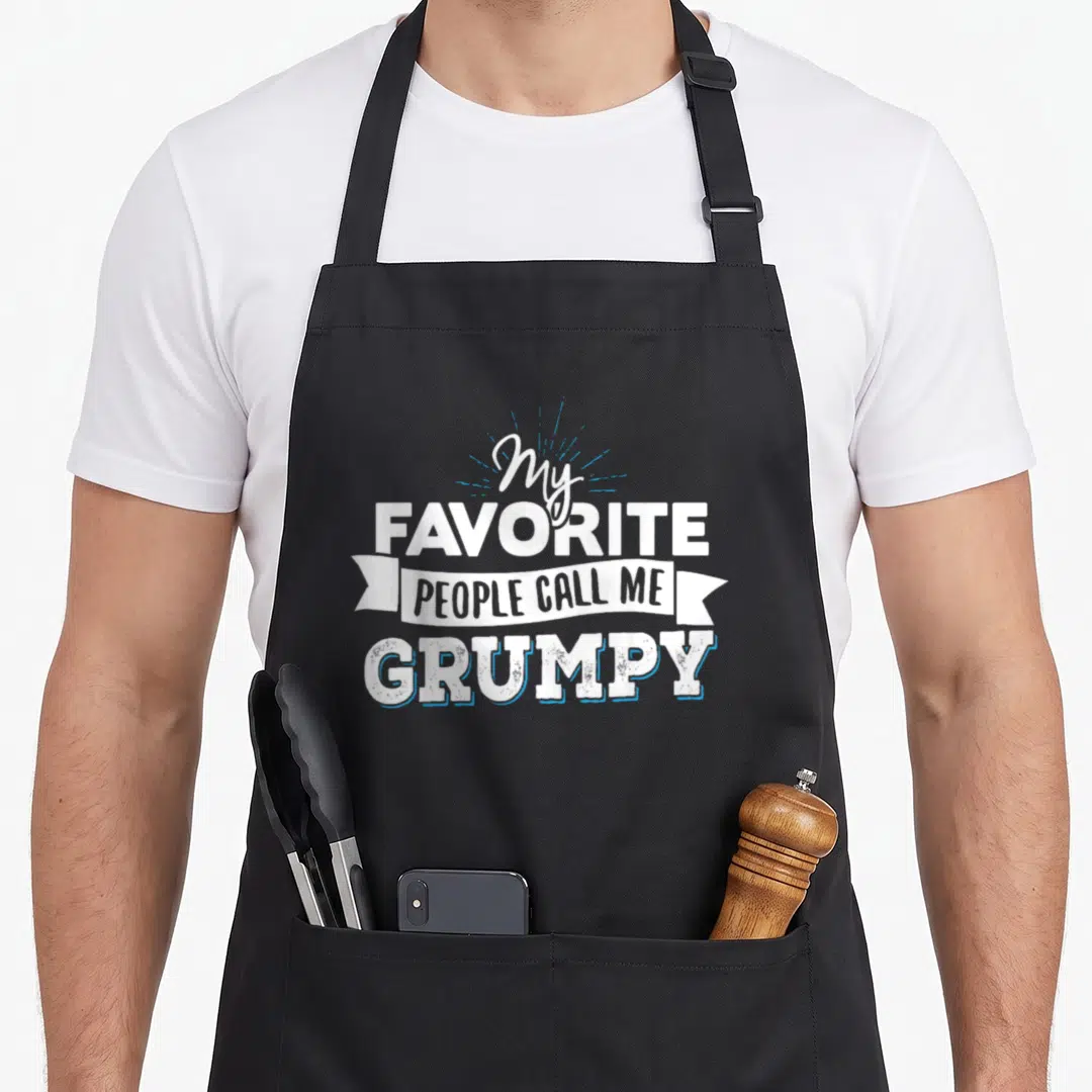 Grumpy grandparent apron - Stacked white text My Favorite People Call Me Grumpy with blue sunburst and ribbon banner — shown on a black cotton canvas apron against a white background
