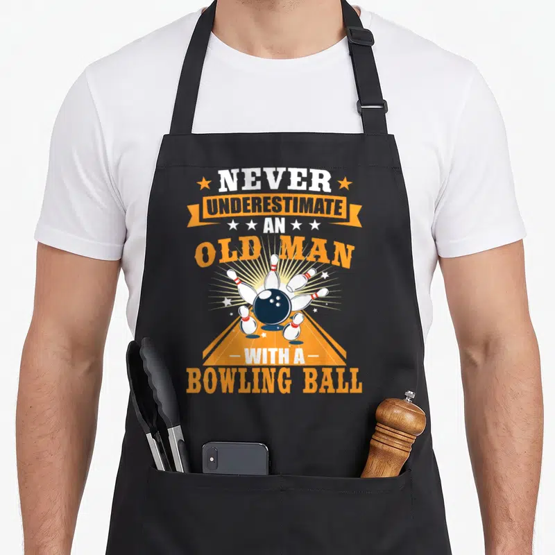 Underestimate bowling apron - Retro text Never Underestimate An Old Man With A Bowling Ball above blue ball and white — shown on a black cotton canvas apron against a white background