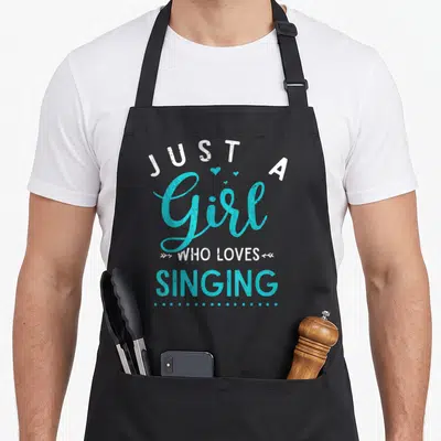 Singing theatre apron - Stacked turquoise and white text reading Just a Girl Who Loves Singing with hearts and arrows — shown on a black cotton canvas apron against a white background