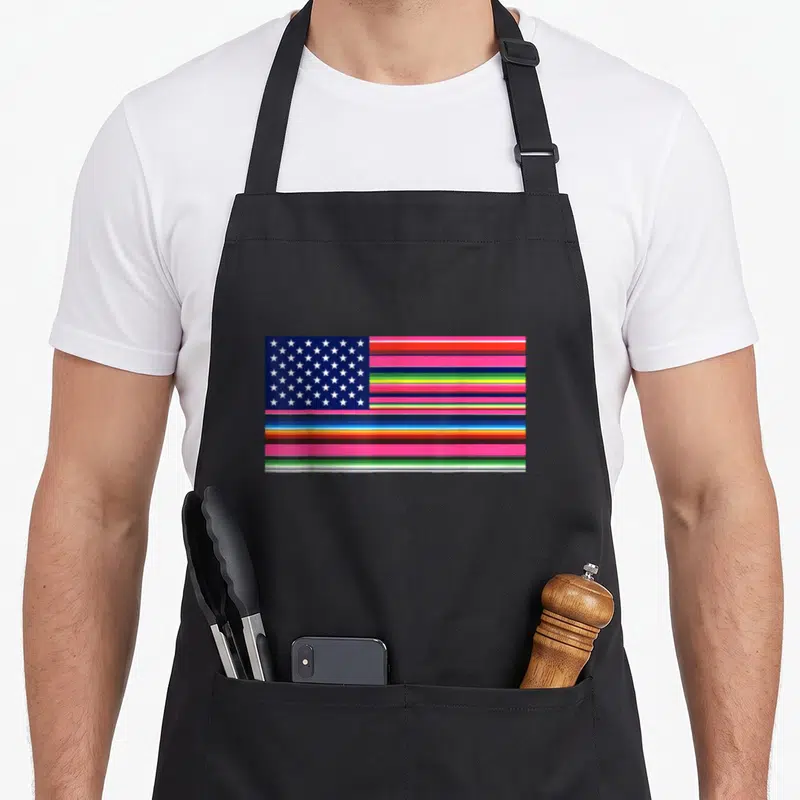 Cinco american flag apron - Rectangular flag with blue star field and pink green yellow red white horizontal stripes — shown on a black cotton canvas apron against a white background