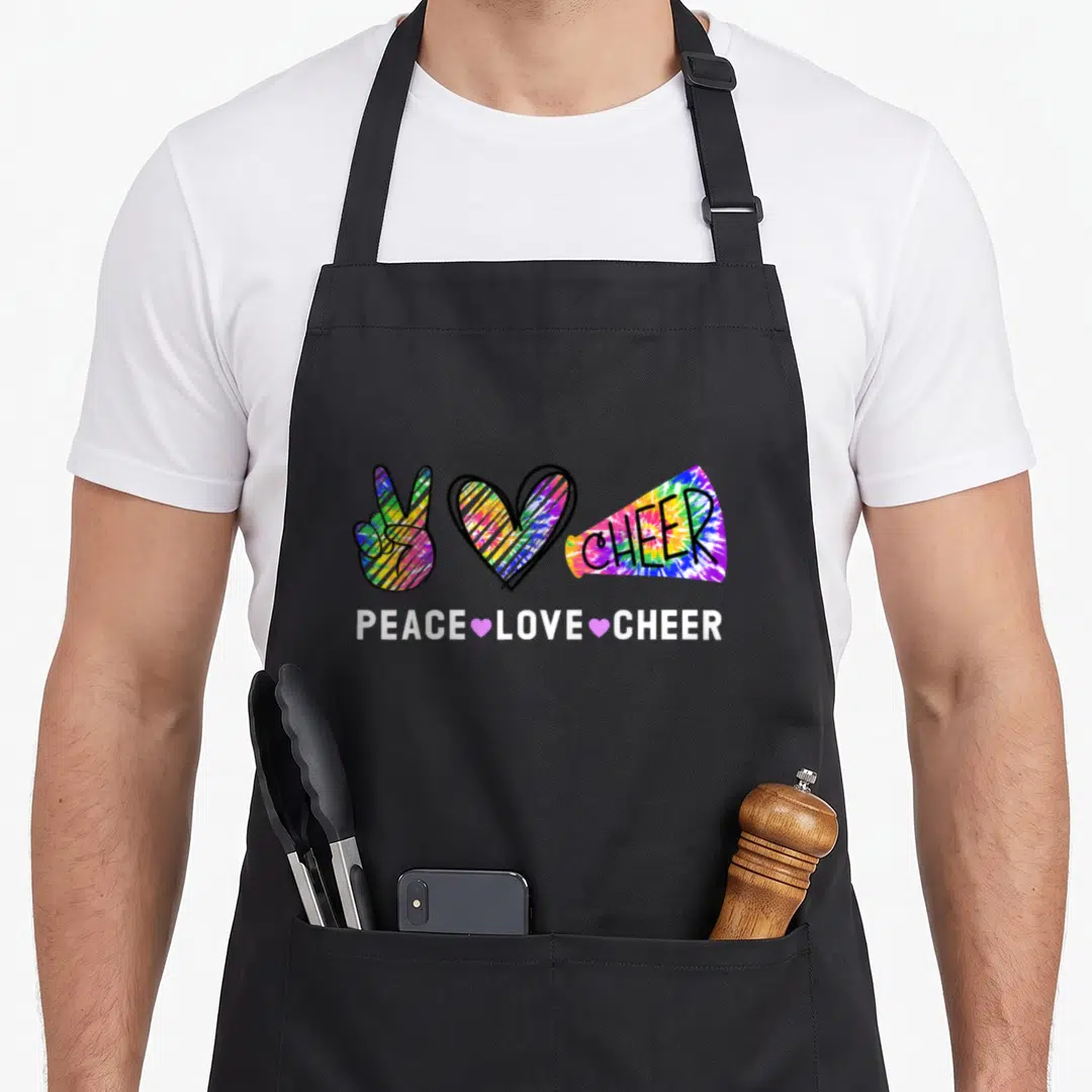 Cheer tie-dye apron - Tie-dye peace sign, heart, and megaphone with PEACE LOVE CHEER text — shown on a black cotton canvas apron against a white background