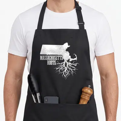 Massachusett patriotic apron - White Massachusetts map outline with tree roots and distressed stacked text reading — shown on a black cotton canvas apron against a white background