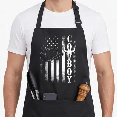 Western southern aprons - White distressed flag with cowboy hat, bull skull, and vertical COBOY text — shown on a black cotton canvas apron against a white background