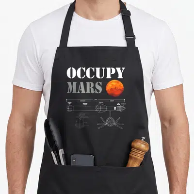 Occupy space houston apron - OCCUPY MARS text with technical rocket diagram showing 118 M measurement and component — shown on a black cotton canvas apron against a white background