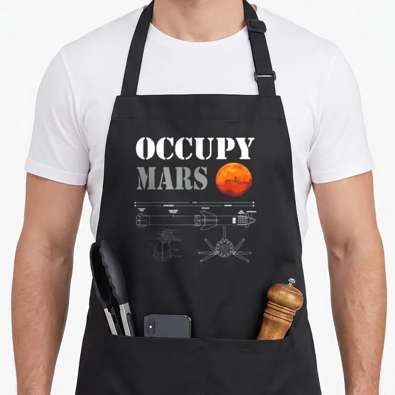 Occupy space houston apron - OCCUPY MARS text with technical rocket diagram showing 118 M measurement and component — shown on a black cotton canvas apron against a white background