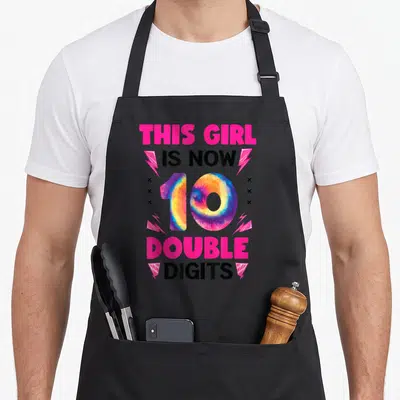 Double tie-dye apron - Stacked text THIS GIRL IS NOW 10 DOUBLE DIGITS with tie-dye number 10 and lightning bolts — shown on a black cotton canvas apron against a white background