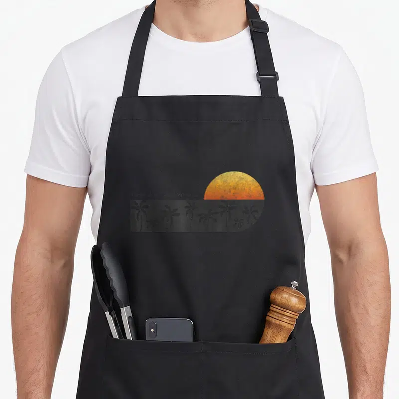 Horseshoe pride apron - Distressed sunset and palm trees with Horseshoe Bay Bermuda text — shown on a black cotton canvas apron against a white background