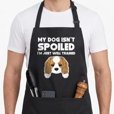 Spoiled king apron - Cartoon brown and white dog head with two paws under three lines of white text reading My Dog — shown on a black cotton canvas apron against a white background