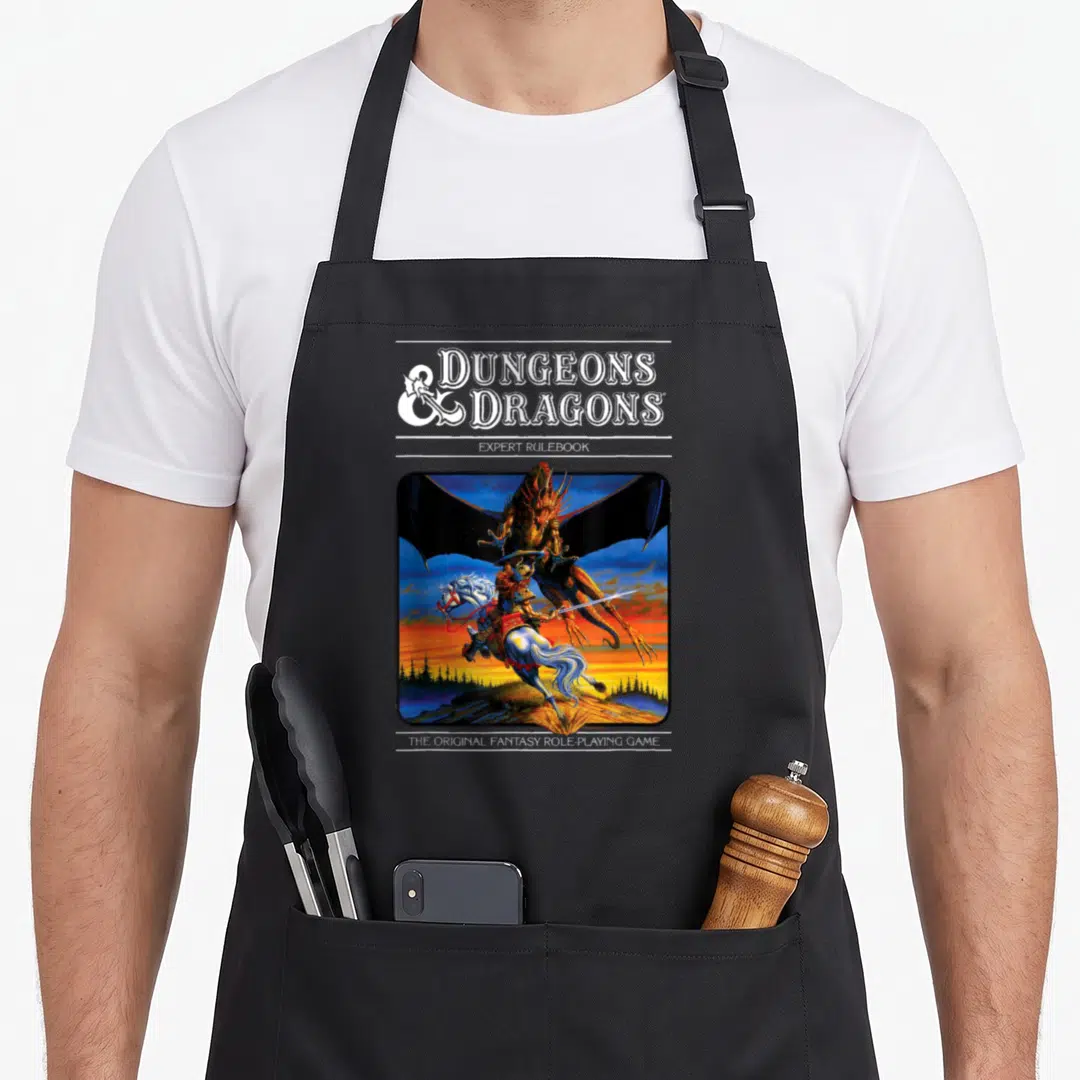 Expert dragon apron - Dungeons & Dragons Expert Rulebook text above a knight fighting a dragon in blue and orange — shown on a black cotton canvas apron against a white background