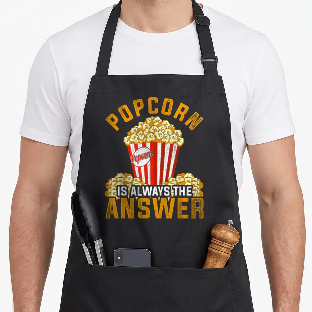 Popcorn watching life apron - Retro orange text POPCORN IS ALWAYS THE ANSWER over red white striped bucket filled — shown on a black cotton canvas apron against a white background
