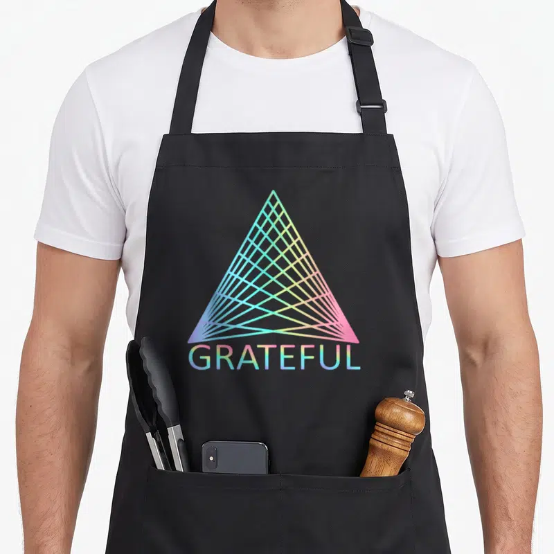 Spiritual trinity apron - Gradient triangle with blue pink and yellow lines above GRATEFUL text — shown on a black cotton canvas apron against a white background